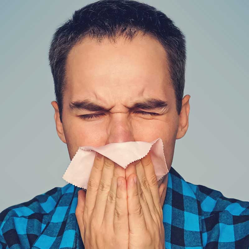 Man blowing nose in attempt to relieve his allergies. 